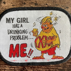 May include: Embroidered patch with a black border and the text "MY GIRL HAS A DRINKING PROBLEM... ME!!" in black and red. A cartoon figure in yellow and red clothing is holding a drink.