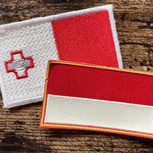 May include: Two rectangular patches featuring national flags. One patch displays the white and red vertical bicolor flag of Malta with a George Cross in the upper left corner. The other patch shows the red and white horizontal bicolor flag.