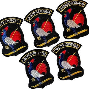 May include: Five embroidered patches with a black background, featuring a rooster with blue, white, and red details. Each patch has a yellow border and a curved top with text, including "LES ARCS" and "LA BRESSE VOSGES".