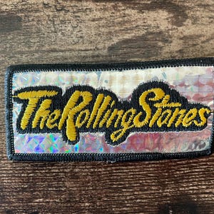 Könnte beinhalten: Eine weiße Keramik-Tasse mit schwarzem Henkel und dem Text "But First, Coffee" in fetter, schwarzer Schrift. Die Tasse steht vor einem verschwommenen Hintergrund, der eine gemütliche Umgebung suggeriert.