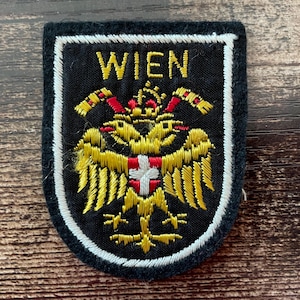 Op de afbeelding: Een set van drie keramische mokken met een gespikkelde, crèmekleurige glazuur. Elke mok heeft een ander handgeschilderd ontwerp: een blauw en groen blad, een gele bloem en een rode bes. De mokken hebben een eenvoudige, afgeronde vorm.