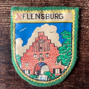 May include: A white ceramic mug with a black handle and the text "But First, Coffee" in a bold, black font. The mug is set against a blurred background, suggesting a cozy setting.