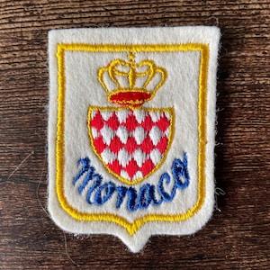 Op de afbeelding: Een witte keramische mok met een zwarte handgreep en de tekst "But First, Coffee" in een vetgedrukte, zwarte letter. De mok staat tegen een vage achtergrond, wat een gezellige setting suggereert.