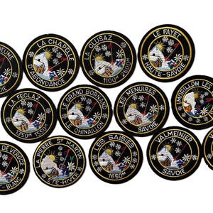 Pode incluir: Uma coleção de doze emblemas bordados circulares com bordas pretas e texto dourado. Cada emblema retrata uma paisagem de montanha nevada com um sol, flocos de neve e um pequeno edifício, representando várias estâncias de esqui francesas.