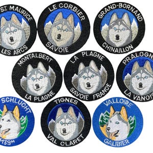 Puede incluir: Una colección de ocho parches bordados circulares con cabezas de perro husky. Cada parche muestra un nombre de lugar en texto blanco sobre un borde negro o azul, con un paisaje de montaña y una cara de husky gris y blanca en el centro.