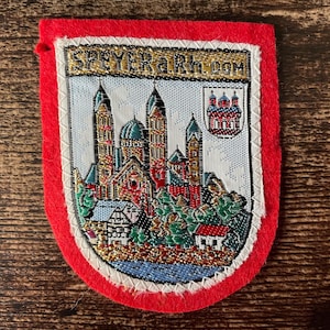May include: Embroidered patch with a red border and a detailed image of a cathedral and buildings. The patch features the text "SPEYERa.Rh.com" in gold lettering. The central image is a colorful depiction of a cityscape.