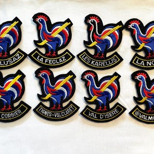 May include: Eight embroidered patches featuring a rooster with crossed skis and the name of a ski resort in France. The patches are black with white, red, blue and yellow embroidery.