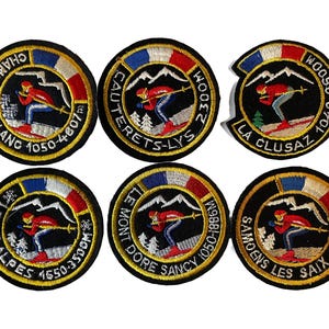 May include: Six embroidered patches with a black background, featuring a skier in red and blue, mountains, and text. Each patch has a circular design with a gold border and a French flag color scheme.