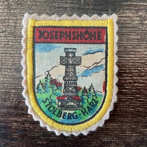 May include: Embroidered patch featuring a detailed illustration of a tower with the text "JOSEPHSHÖHE" at the top and "STOLBERG-HARZ" at the bottom. The patch has a yellow border and a cream-colored scalloped edge.