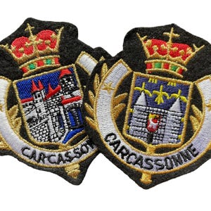 May include: Two embroidered patches featuring the coat of arms of Carcassonne. Each patch displays a red and gold crown above a blue shield with a castle illustration, surrounded by a white banner with the text CARCASSONNE in black thread.