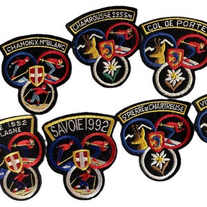 May include: A collection of embroidered fabric patches featuring various French ski resorts and locations. Each patch displays colorful circular designs with skiers, mountain motifs, edelweiss flowers, and regional text like Savoie 1992.