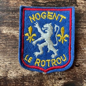 May include: A blue patch with red and yellow trim. The patch features the words "NOGENT" and "LE ROTROU" in yellow, surrounding a white lion and yellow fleur-de-lis symbols.