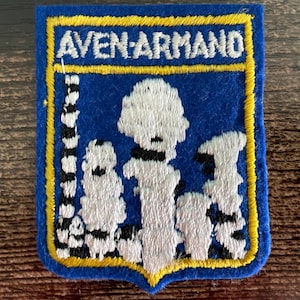 May include: A rectangular blue embroidered patch with a yellow border featuring the white text AVEN-ARMAND at the top. The center displays a white and black graphic illustration of stalagmites and stalactites against a solid blue background.