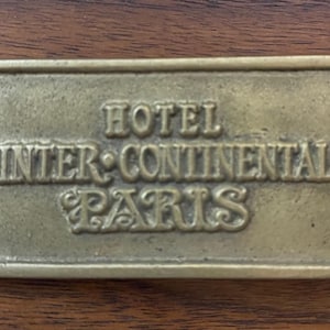 May include: Brass key chain tag with the text "Hotel Inter-Continental Paris" in a vintage style font.