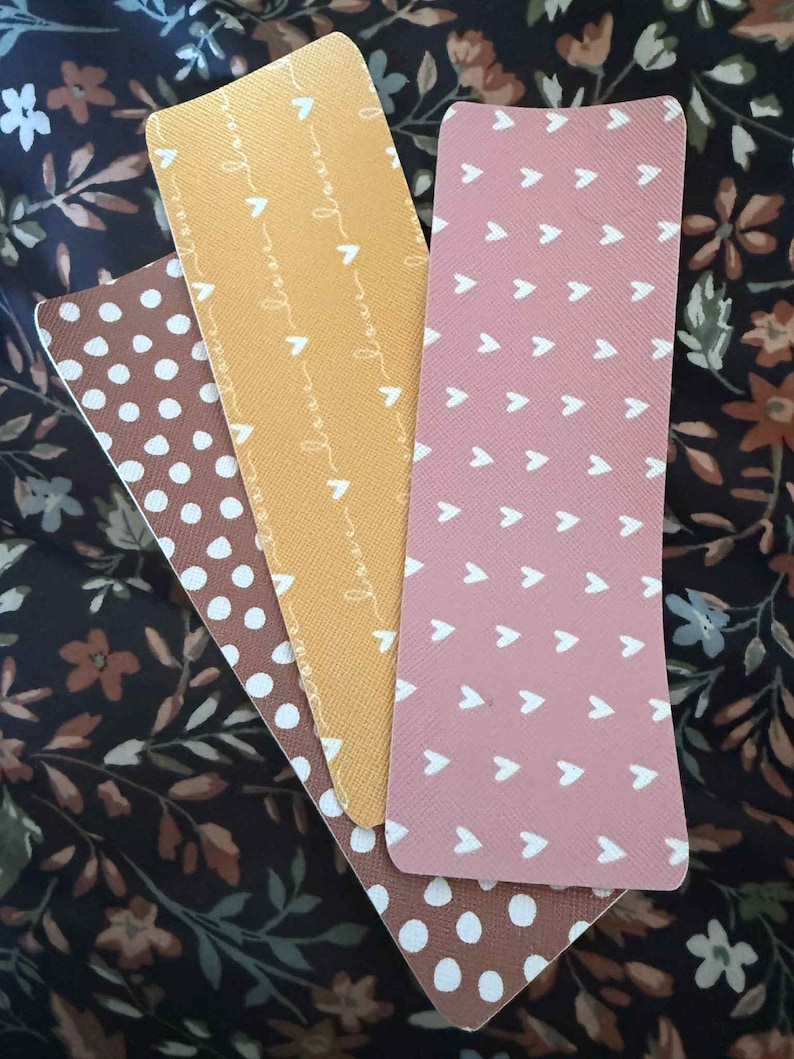 Puede incluir: Cuatro marcap&aacute;ginas rectangulares con varios dise&ntilde;os. Uno es marr&oacute;n con lunares blancos, otro es amarillo con la palabra "love" repetida, un tercero es rosa con flechas blancas y el &uacute;ltimo es marr&oacute;n con lunares blancos.