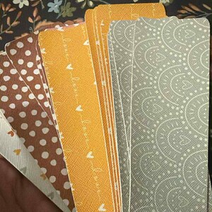 Puede incluir: Un conjunto de cartas de tarot con varios dise&ntilde;os. Las cartas presentan patrones como lunares, cachemir y una escritura repetida "love". Los colores incluyen marr&oacute;n, amarillo y gris. El fondo es un patr&oacute;n floral oscuro.