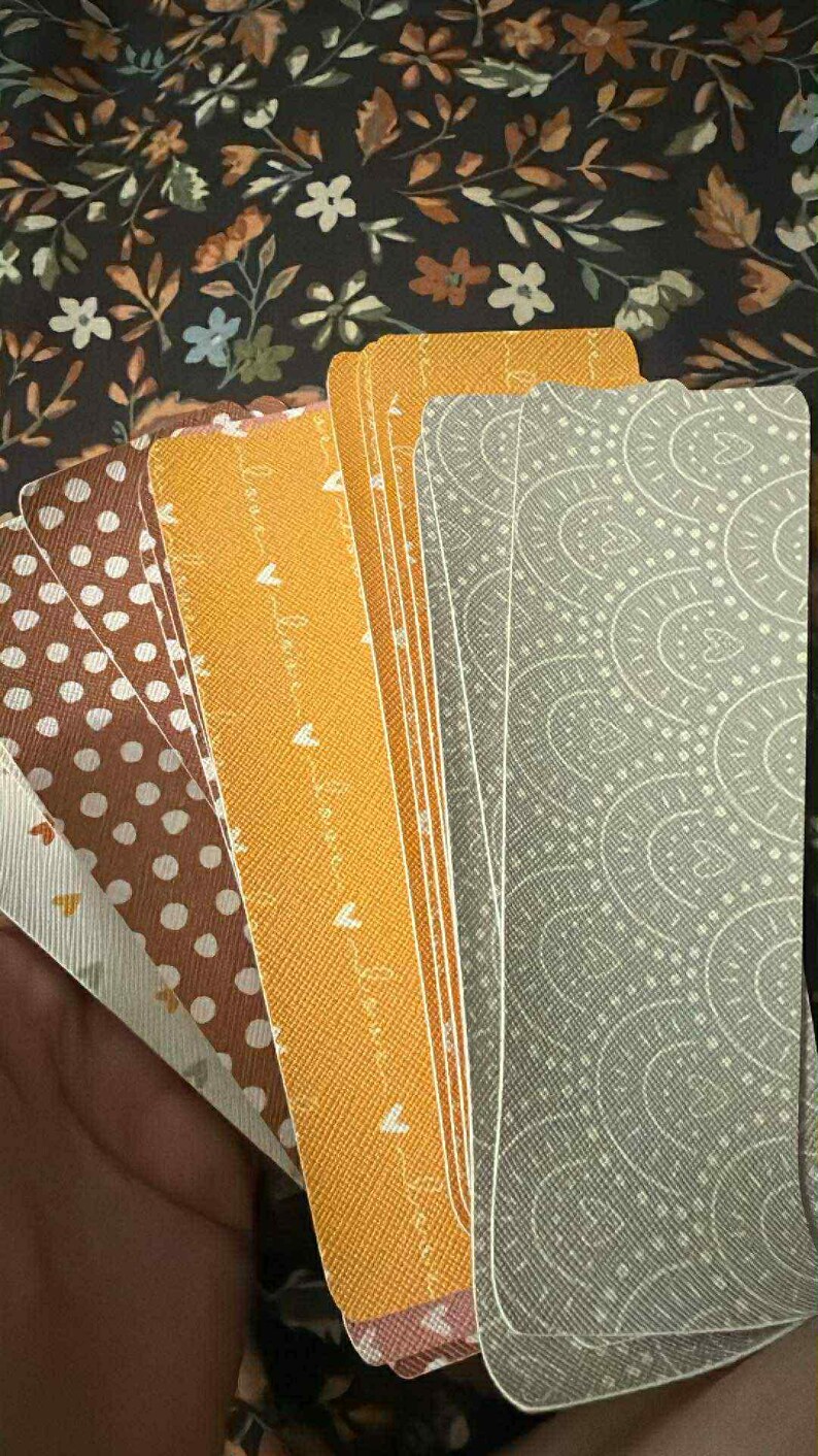 Puede incluir: Un conjunto de cartas de tarot con varios dise&ntilde;os. Las cartas presentan patrones como lunares, cachemir y una escritura repetida "love". Los colores incluyen marr&oacute;n, amarillo y gris. El fondo es un patr&oacute;n floral oscuro.