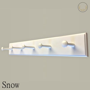 May include: White wooden coat rack with five hooks. The rack is mounted on a wall and has a simple, modern design. The word "Snow" is printed below the rack.