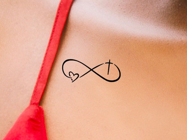 May include: A black infinity symbol tattoo with a heart and a cross inside. The tattoo is on a person's shoulder.