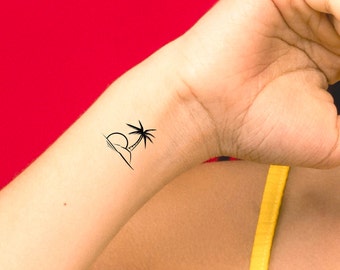 May include: A simple black line drawing of a palm tree on a beach with a sun setting behind it. The tattoo is on a person's wrist.