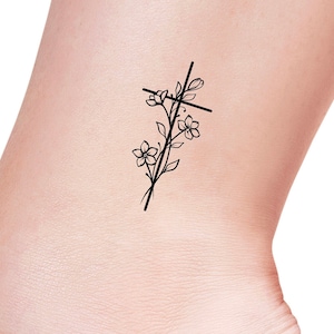 May include: A black line drawing tattoo design of a cross with flowers growing around it.