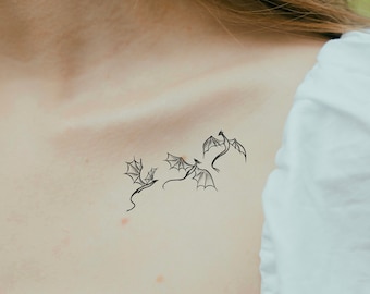 May include: A close-up of a person's collarbone with a black temporary tattoo of three stylized dragons flying in a row.