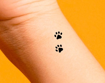 May include: Two black paw print tattoos on a person's wrist.