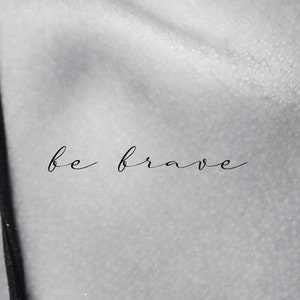 May include: A black and white image of the phrase "be brave" written in cursive script.