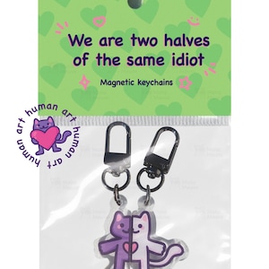 May include: A pair of magnetic keychains with a split cat design, one half purple, the other white. The keychains are packaged with a green backing that reads "We are two halves of the same idiot." and "Magnetic keychains."