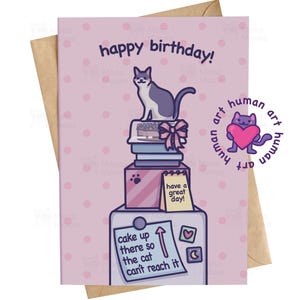 Könnte beinhalten: Geburtstagskarte mit einer Cartoon-Katze auf einem Kuchen und Büchern, mit dem Text "happy birthday!". Die Karte hat auch den Satz "cake up there so the cat can't reach it". Die Karte ist hellrosa und wird mit einem braunen Umschlag geliefert.