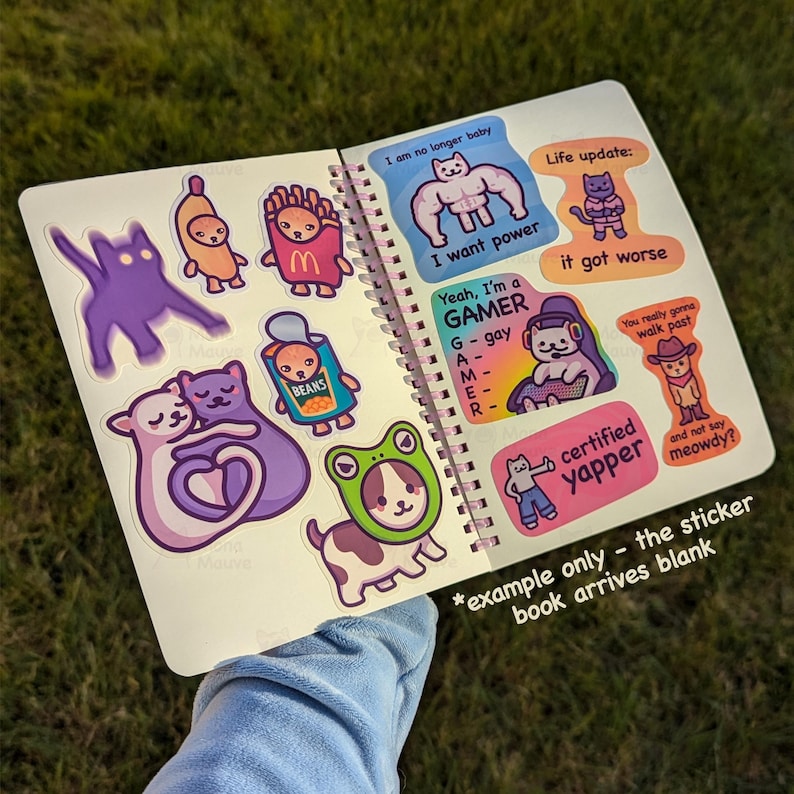 May include: Open notebook with colorful stickers. Stickers include a purple cat, a banana, a french fry, a can of beans, a cat with a frog hat, and text that says "I want power", "Yeah, I'm a GAMER", and "certified yapper".