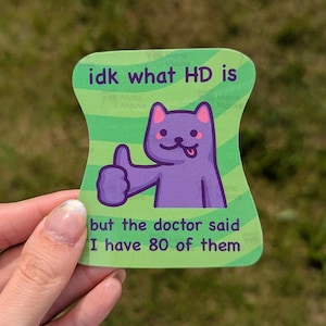 May include: A die-cut sticker with a light green background featuring wavy stripes and a purple cartoon cat giving a thumbs up. The text reads: idk what HD is but the doctor said I have 80 of them. The sticker has a unique, curved shape.