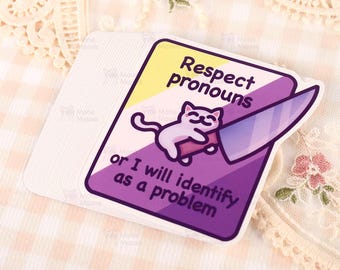 Op de afbeelding: Een stapel stickers met een ontwerp met een kat die een mes vasthoudt. De sticker heeft een paars, geel en wit kleurenschema met de tekst "Respect pronouns or I will identify as a problem."