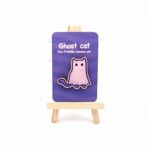 Può includere: Uno spillo in legno di colore viola e bianco con un gatto fantasma su uno sfondo viola con il testo "Ghost cat" e "Eco-friendly wooden pin".