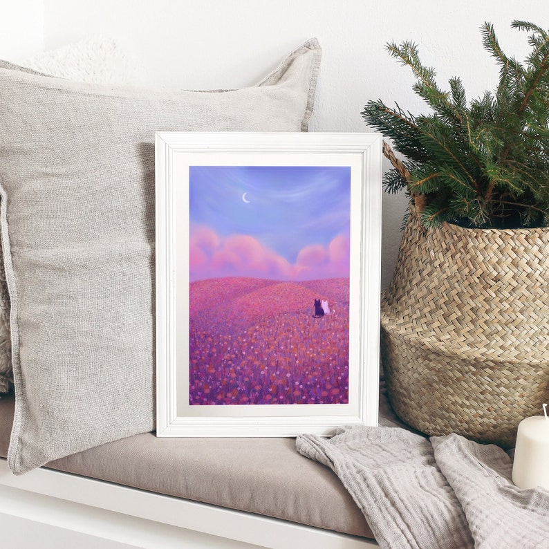 May include: A white framed print of a digital painting depicting two cats sitting in a field of purple flowers under a crescent moon. The sky is a gradient of pink and purple.