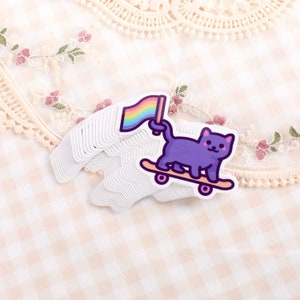 May include: A purple cat with a rainbow flag on a skateboard. The cat is wearing a white collar and has a pink nose.