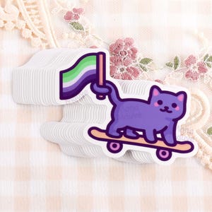 Puede incluir: Una pila de pegatinas troqueladas que muestran un gato morado de dibujos animados sobre un monopatín. El gato sostiene con la cola una bandera con franjas horizontales verdes, blancas y moradas. El diseño tiene un borde blanco y estilo gráfico.