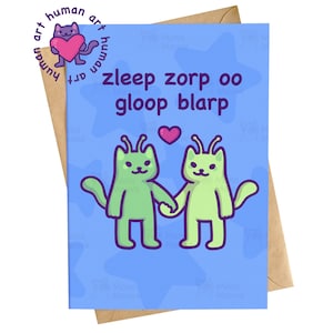 May include: A rectangular greeting card with a light blue background featuring a pattern of faint blue stars. The card displays two light green alien cat figures holding hands, a small pink heart, and the text zleep zorp oo gloop blarp.