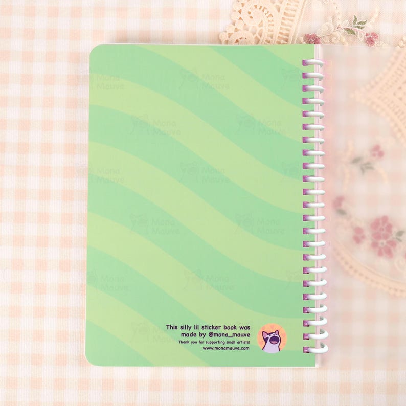 May include: A spiral-bound sticker book with a light green cover featuring diagonal stripes. The text "This silly lil sticker book was made by @mona_mauve" is printed on the bottom. A cartoon cat logo is also visible.