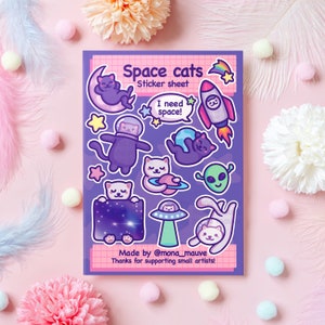May include: A sticker sheet with a purple background featuring space cats in various poses. The sheet includes a cat in a spacesuit, a cat riding a rocket, a cat sleeping on a crescent moon, and a cat holding a planet. The text "Space cats" and "Sticker sheet" is at the top of the sheet. The text "I need space!" is in a speech bubble. The text "Made by @mona_mauve" and "Thanks for supporting small artists!" is at the bottom of the sheet.
