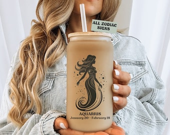 Könnte beinhalten: Ein brauner wiederverwendbarer Becher mit Bambusdeckel und einer Schwarzweißillustration einer Meerjungfrau. Der Becher trägt den Text "Aquarius January 20 - February 18" und einen Aufkleber mit der Aufschrift "All Zodiac Signs".