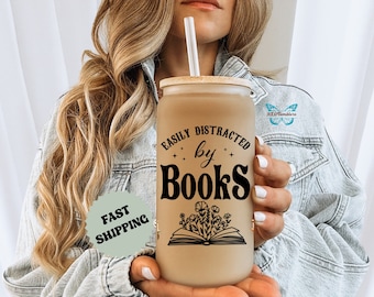May include: A brown and beige reusable tumbler with a black and white design that says "Easily Distracted by Books" with a drawing of a book and flowers.