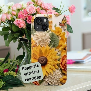 May include: A phone case with a floral design featuring sunflowers, butterflies, and other flowers. The case is white with a black border and supports wireless charging. The text "Supports wireless charging" is written on a green sticker.