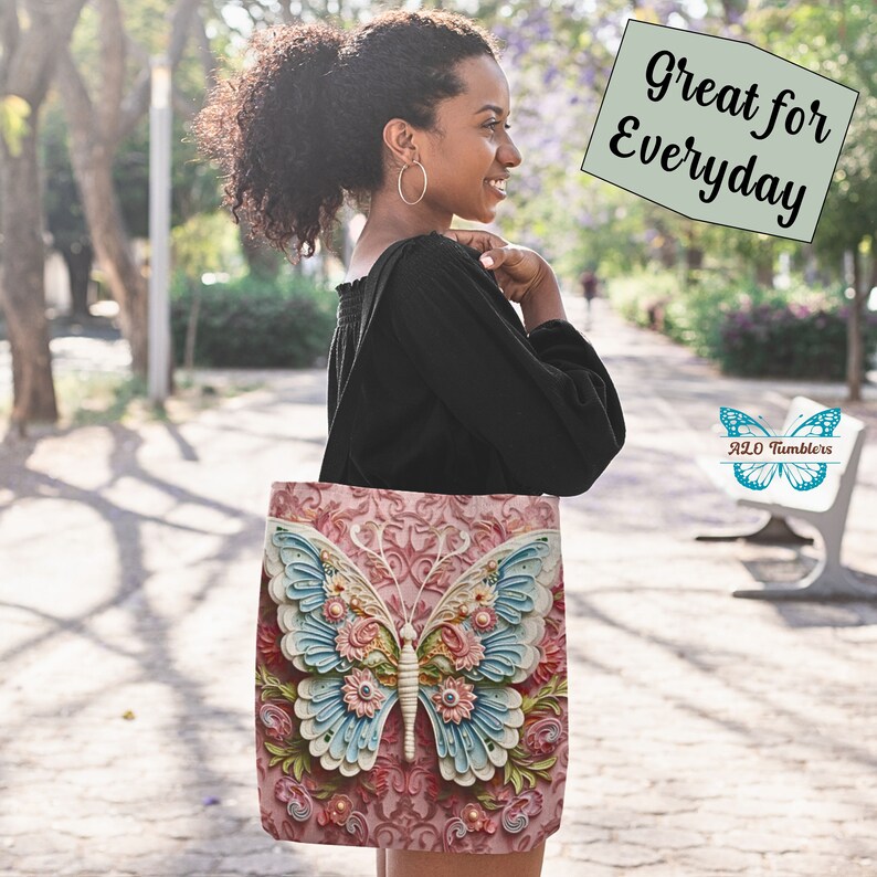 K&ouml;nnte beinhalten: Eine Tragetasche mit einem detaillierten Schmetterlingsdesign. Der Schmetterling hat hellblaue und wei&szlig;e Fl&uuml;gel, verziert mit rosa und gelben Blumen, vor einem rosa floralen Hintergrund. Auf der Tasche steht "Great for Everyday".
