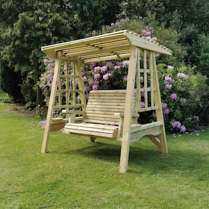 May include: A light-coloured wooden garden swing bench featuring a slatted seat and backrest, suspended by chains from a sturdy frame with a slatted roof canopy and integrated side armrests, positioned on a green lawn in an outdoor setting.
