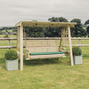 May include: A wooden garden swing bench with a slatted back and seat, suspended by metal chains from a sturdy frame with a roof. The bench features a long, rectangular green cushion. Two light green square planters sit on either side.