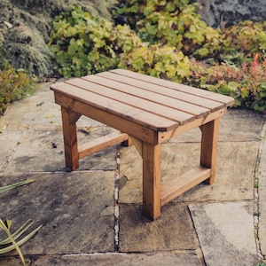 May include: A wooden table with a natural brown finish. The table has a rectangular top with a slightly rounded edge and four legs. The table is sitting on a stone patio.