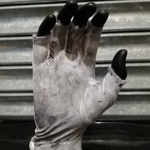 May include: A white cotton glove with black fingertip covers. The glove is worn and has a faded appearance.