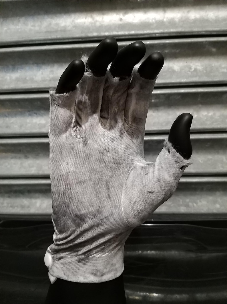 May include: A white cotton glove with black fingertip covers. The glove is worn and has a faded appearance.