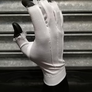 May include: A white cotton glove with a seam down the middle of each finger. The glove is on a black mannequin hand.